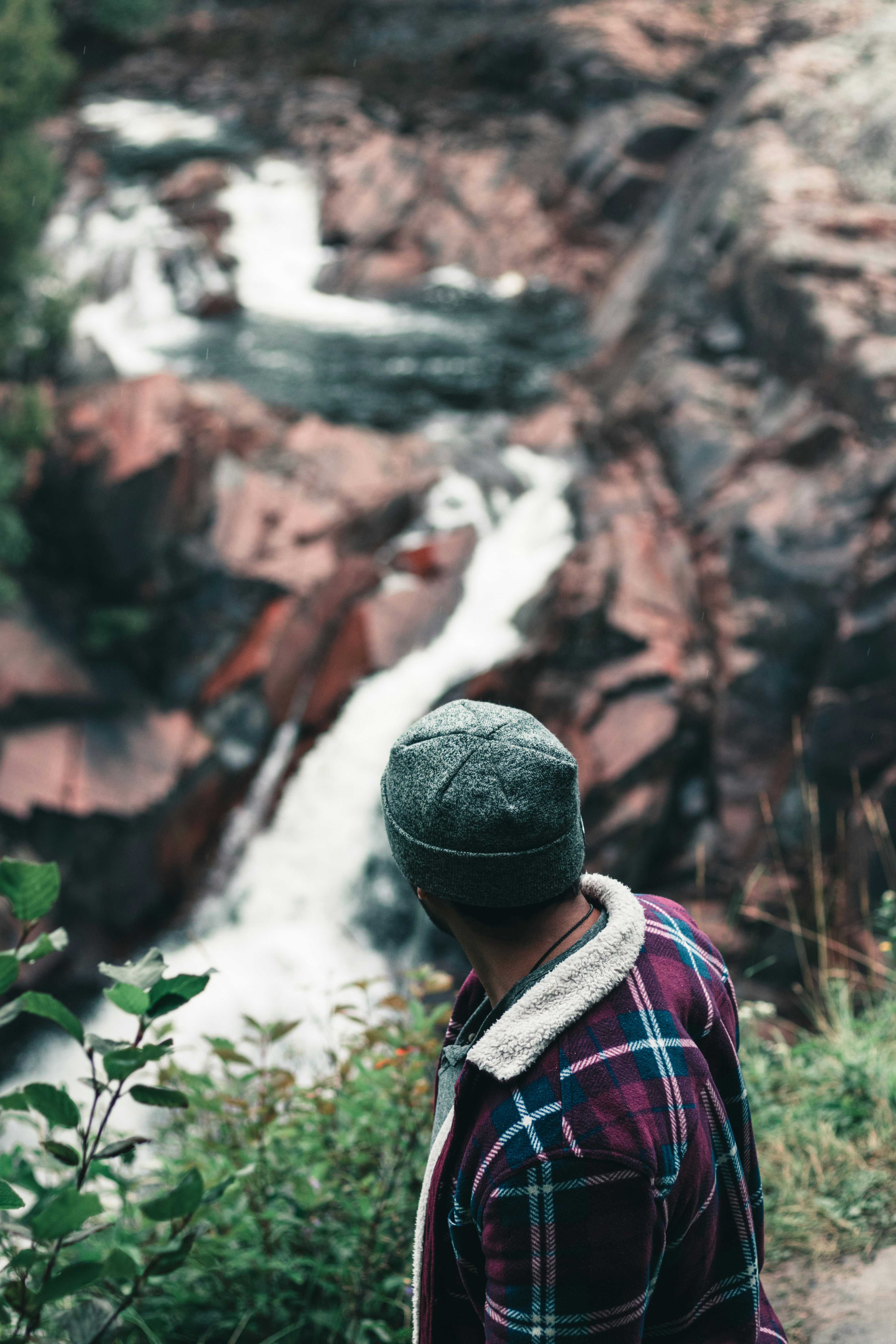 man in red and white plaid shirt wearing black knit cap standing near brown rock formation